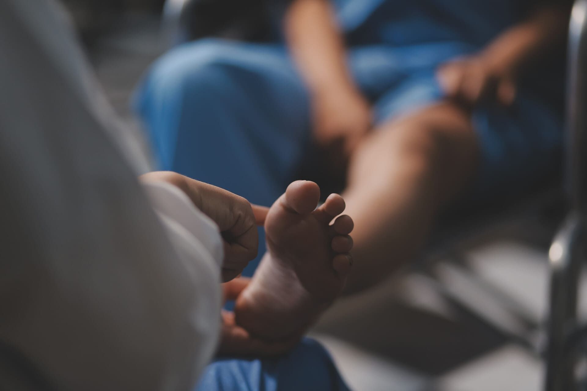 Un trabajador sanitario sostiene el pie de un paciente en un entorno hospitalario borroso.