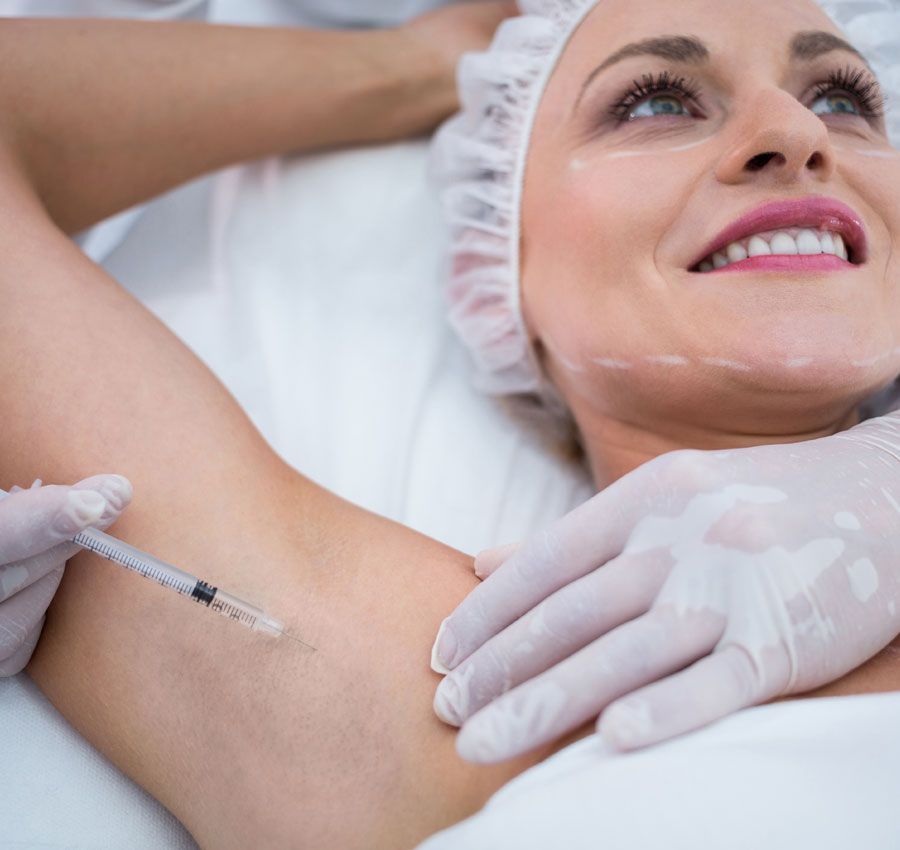 Mujer recibiendo una inyección en la axila, tumbada en una mesa. Un profesional médico sostiene la jeringa.