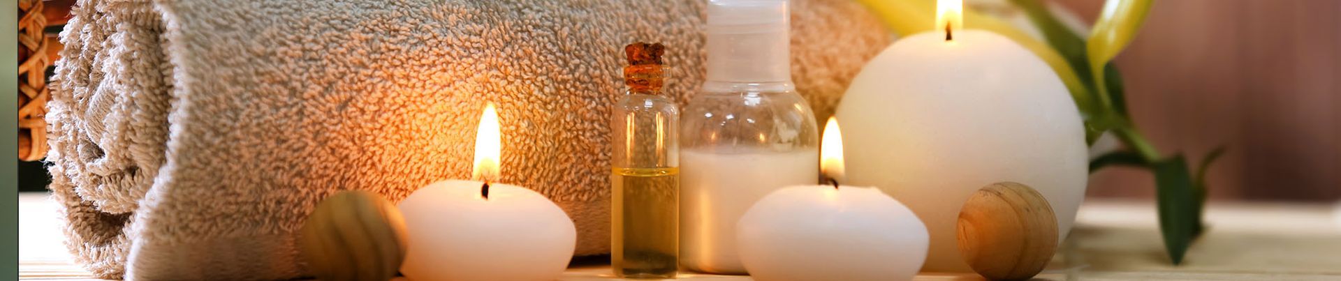 Spa-Stillleben mit brennender Kerze, Fläschchen mit ätherischem Öl, weißen Steinen und einer weißen Orchidee auf einer Holzoberfläche