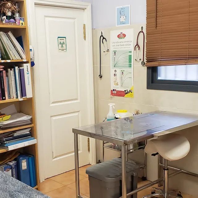 Un consultorio médico con una mesa de acero inoxidable y un taburete.