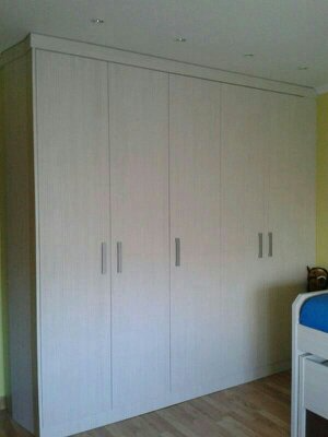 Hay un gran armario blanco en un dormitorio al lado de una cama.