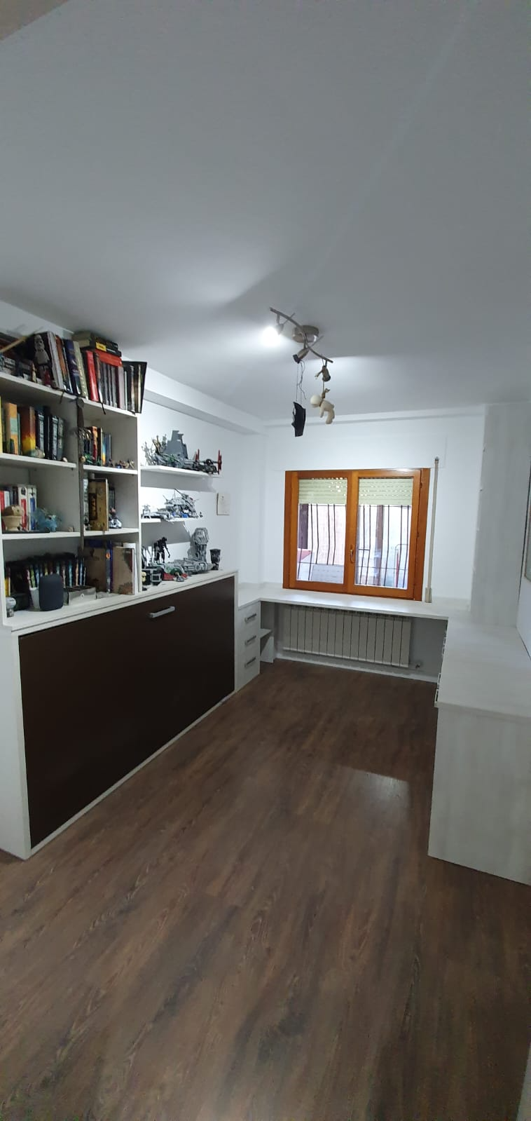 Una habitación con muchos libros en los estantes y una ventana.
