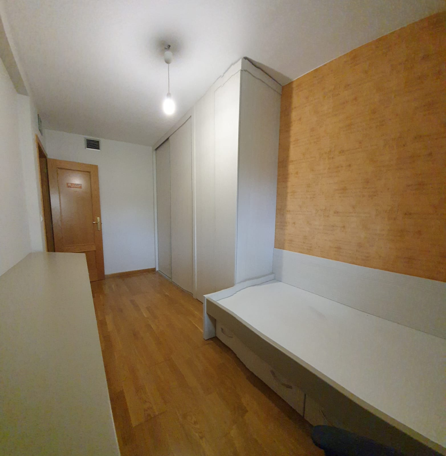 Un dormitorio con pisos de madera y una cama blanca.