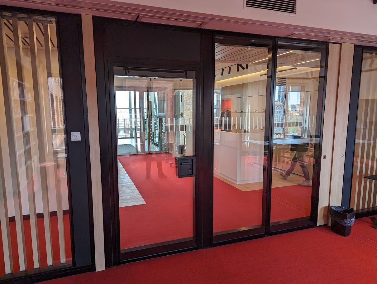 Glastüren mit dunklen Rahmen öffnen sich zu einem Ladeninneren mit rotem Teppichboden.