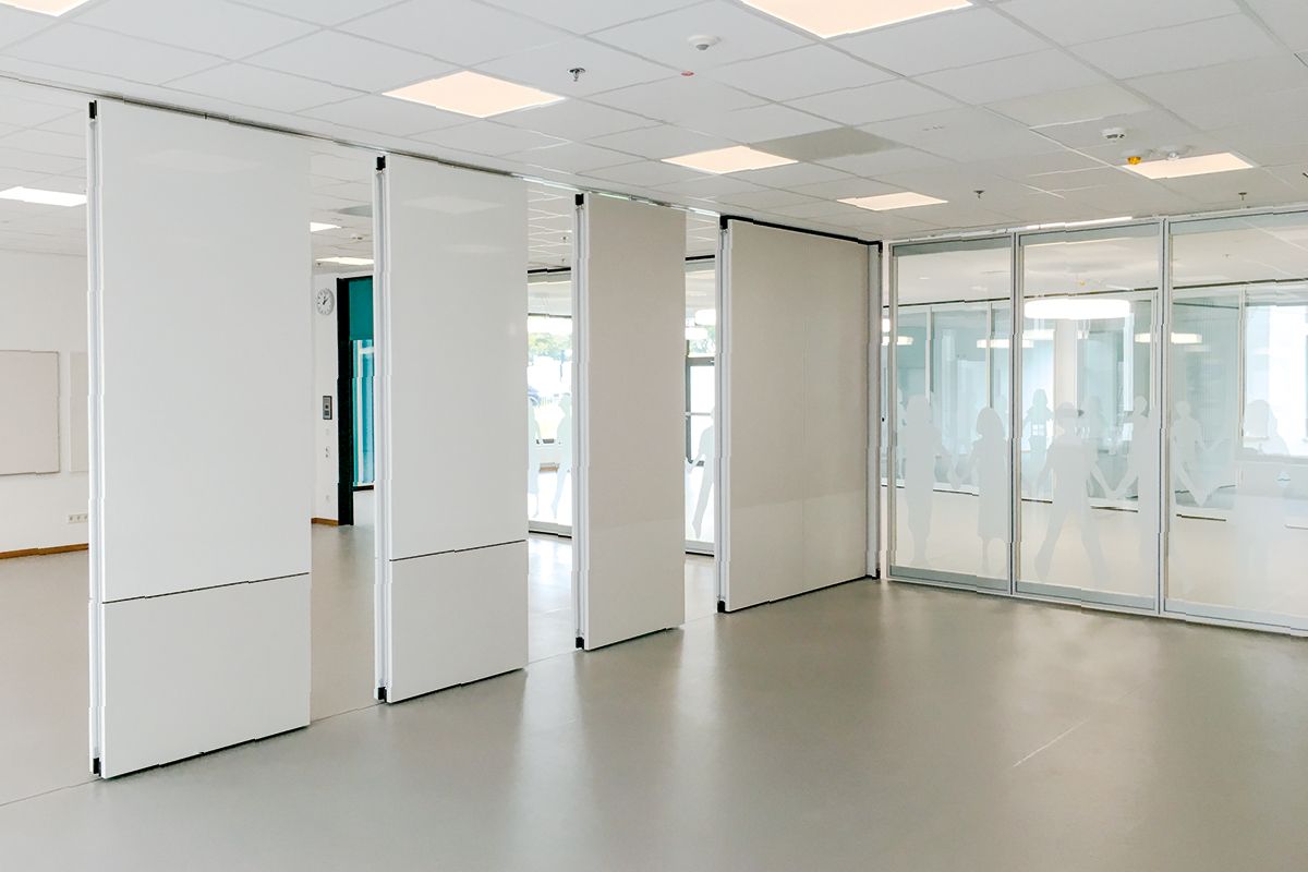 Vier weiße Schiebewände trennen Bereiche in einem hell erleuchteten Büroraum.