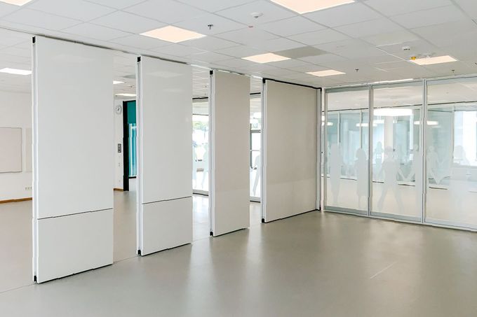 Weiße, bewegliche Trennwände unterteilen einen Raum mit grauem Boden und grauer Deckenbeleuchtung.