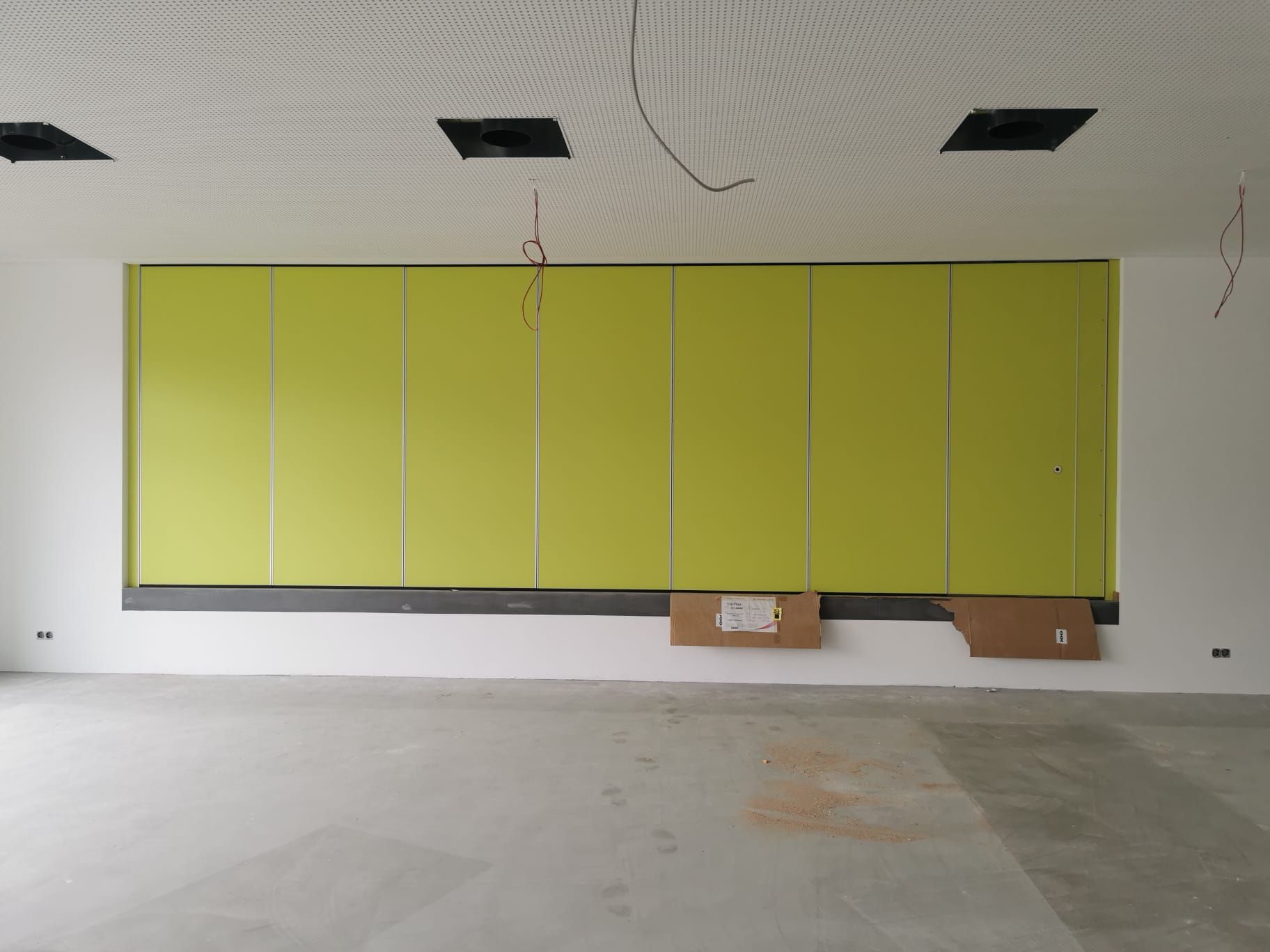 Innenraum eines Zimmers mit großer, lindgrüner Paneelwand, unfertigem Fußboden und weißer Decke mit eingelassenen Quadraten.