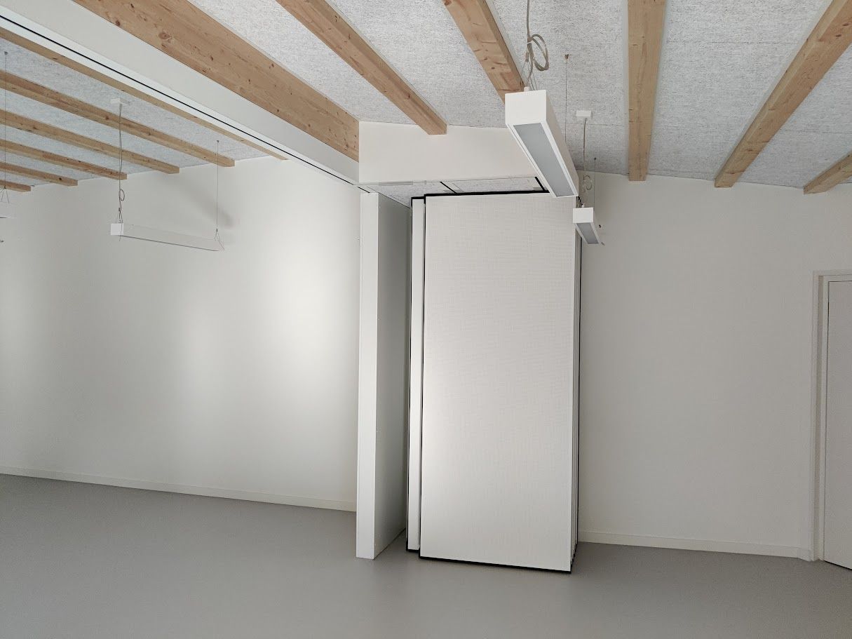 Leerer weißer Raum mit sichtbaren Holzbalken an der Decke und grauem Boden. Große weiße Tür einen Spalt breit geöffnet.