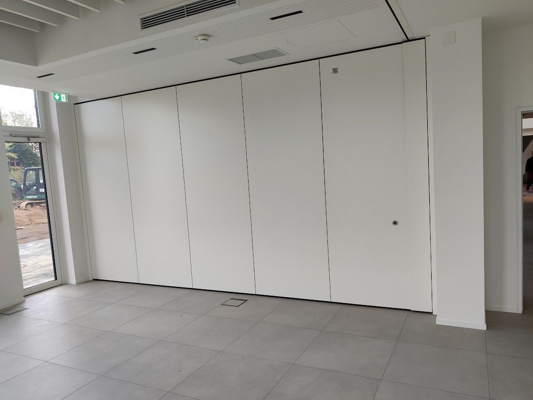 Weiße Faltwand in einem Zimmer, die einen Tür- und Fensterdurchgang teilweise verdeckt. Grauer Fliesenboden.
