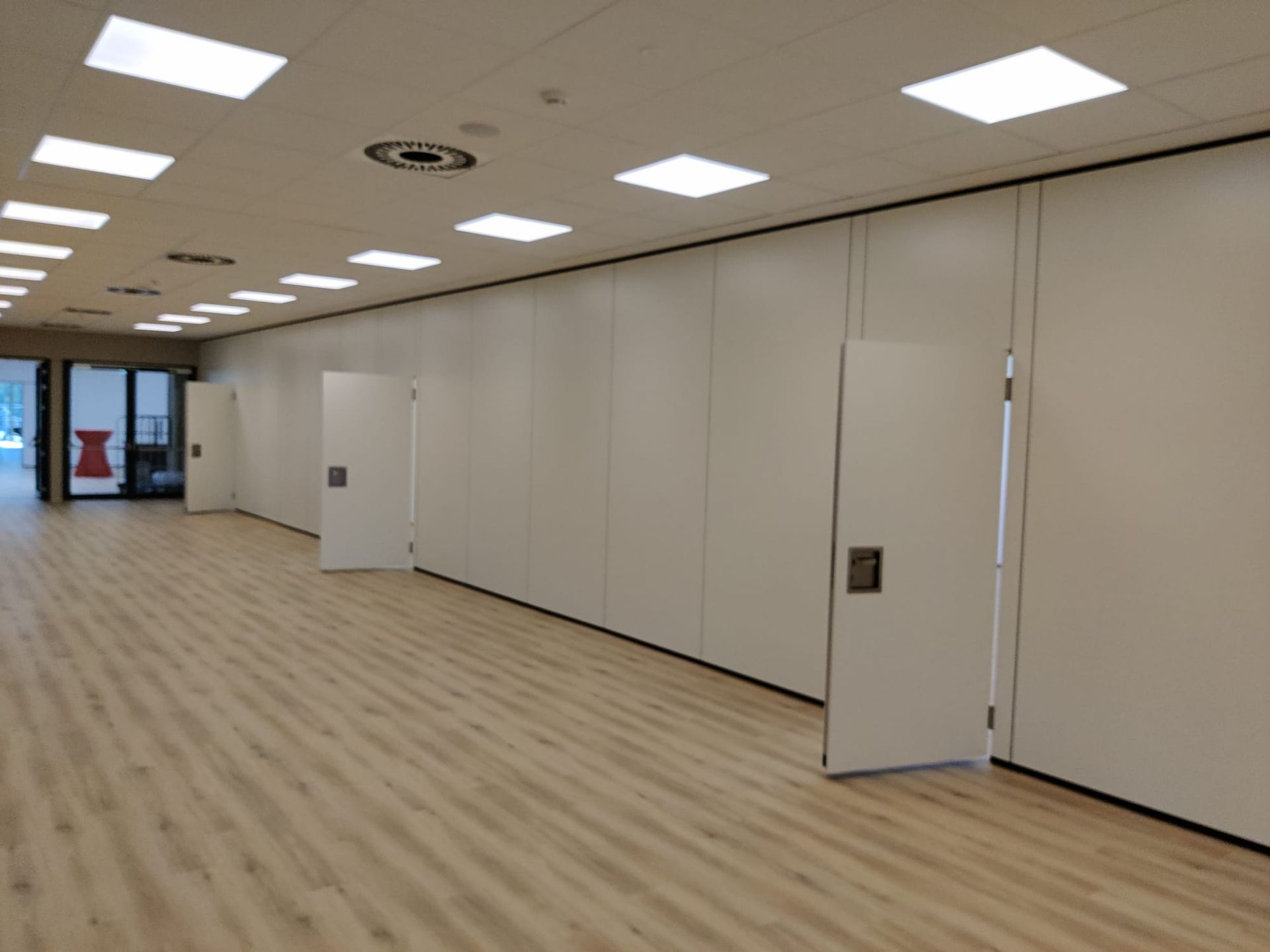 Weiße Modulwände in einem großen Raum mit Holzboden und Deckeneinbaustrahlern. Ein Wandsegment dient als Tür.