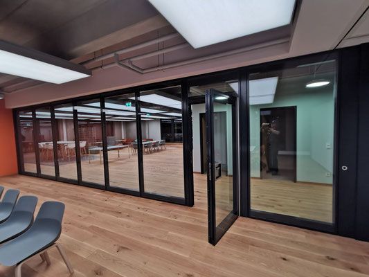 Konferenzraum mit Glastüren, Holzboden und schwarzen Zierleisten. Stühle stehen im Vordergrund.