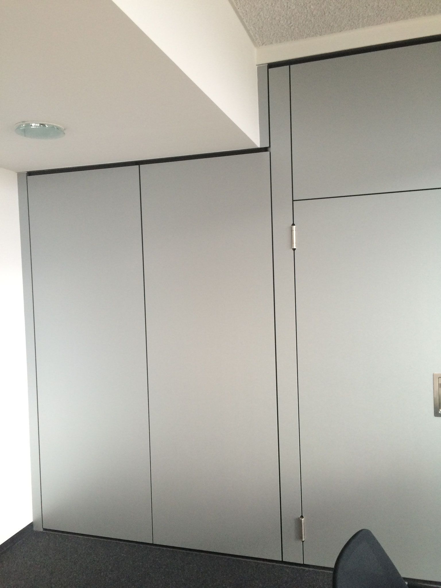 Wandpaneele aus Milchglas in einem Raum. Schwarzer Rahmen, dunkler Teppich, weiße Decke.