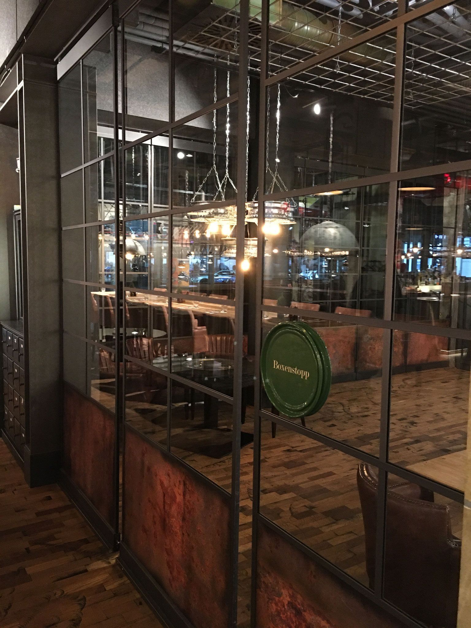 Das Restaurantinterieur, gesehen durch eine Trennwand aus Metall und Glas, Backsteinwände und gedämpftes Licht.