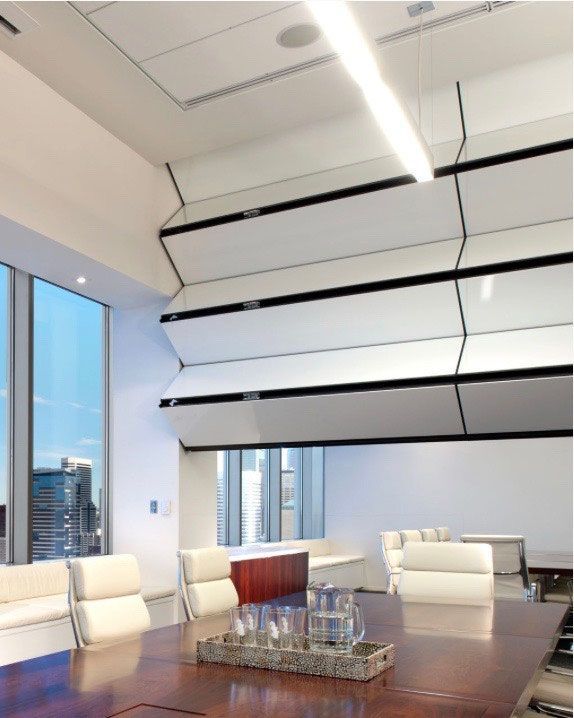 Moderner Bürokonferenzraum mit großem Holztisch und automatisierten Wandpaneelen. Hohe Fenster bieten einen Blick auf die Stadt.