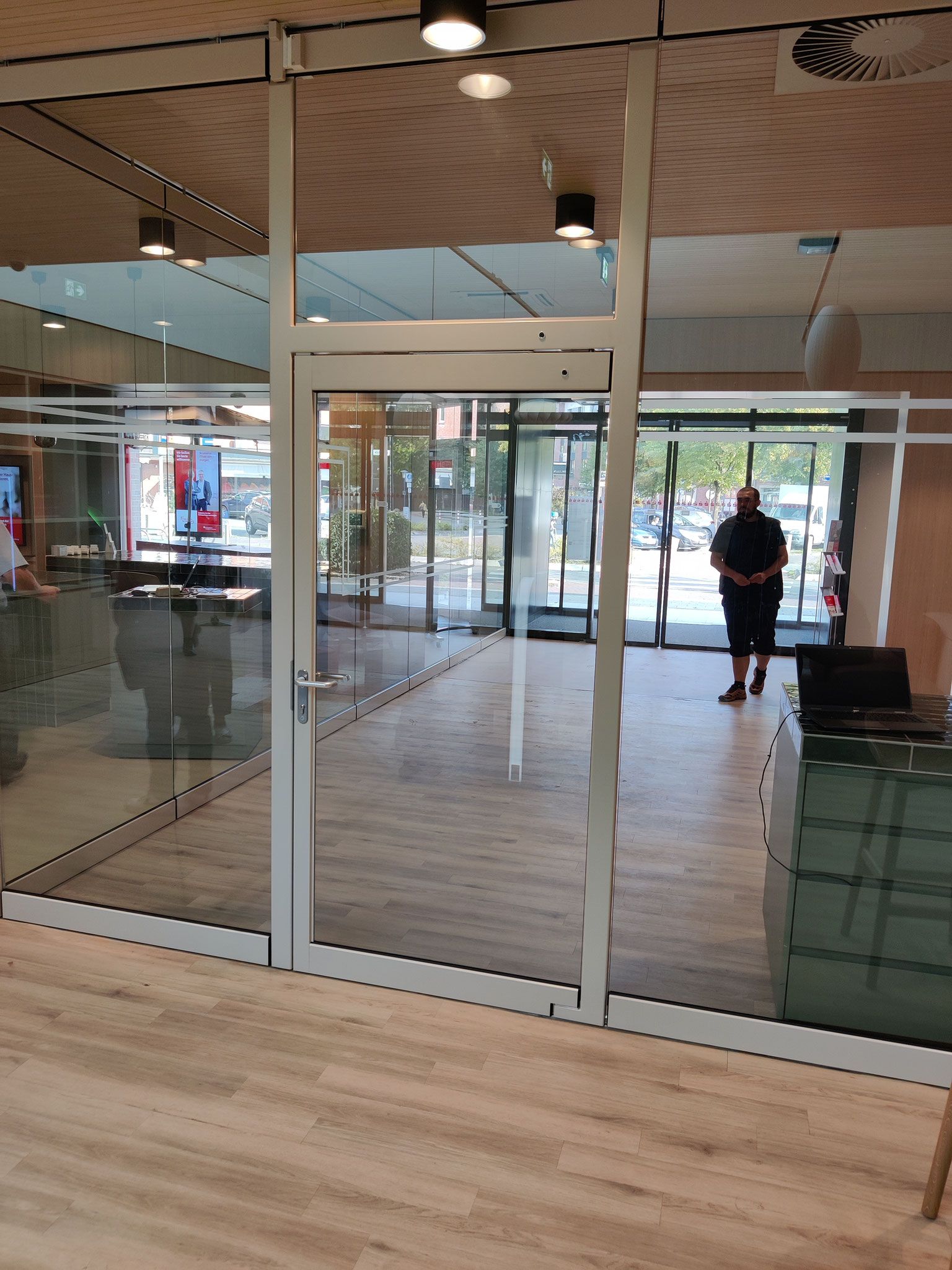 Verglaster Raum mit Tür. Draußen steht eine Person. Natürliches Licht, Holzboden.