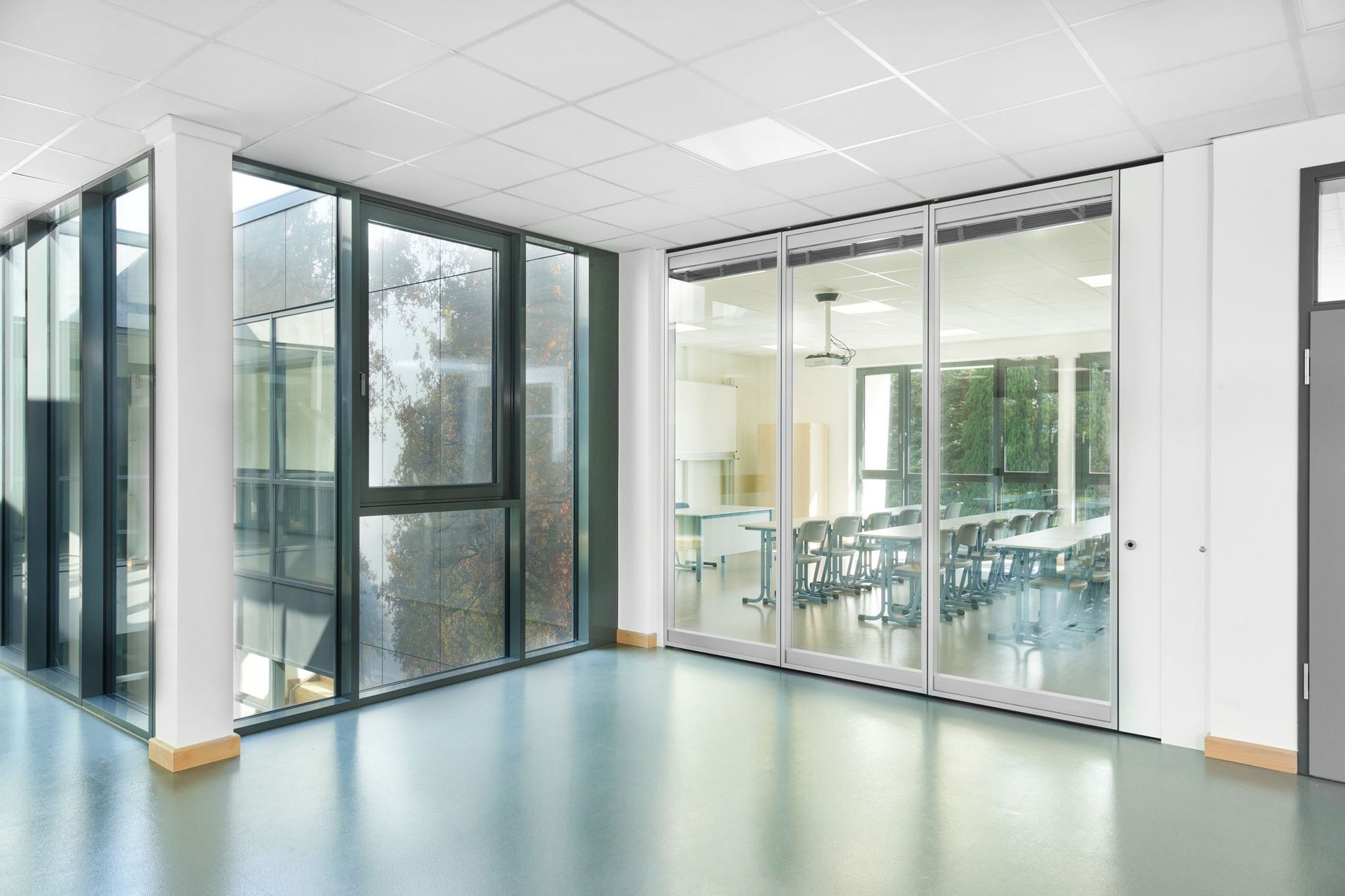 Innenansicht eines modernen Gebäudeflurs mit großen Glasfenstern und einer Tür, die zu einem Konferenzraum führt.
