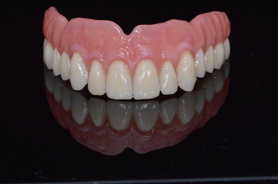 Juego de dentaduras postizas con dientes blancos y encías rosadas reflejadas sobre una superficie negra.