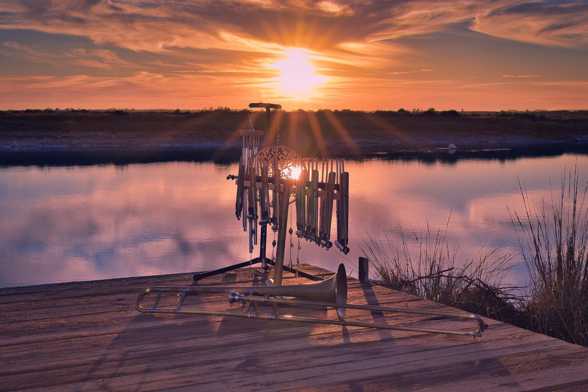 Puesta de sol sobre un lago en calma, con un muelle de madera y una valla reflejados en el agua de color rosa anaranjado.