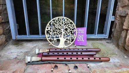Adorno metálico con forma de árbol, con tubos rojos y una etiqueta morada, apoyado contra una pared enrejada.