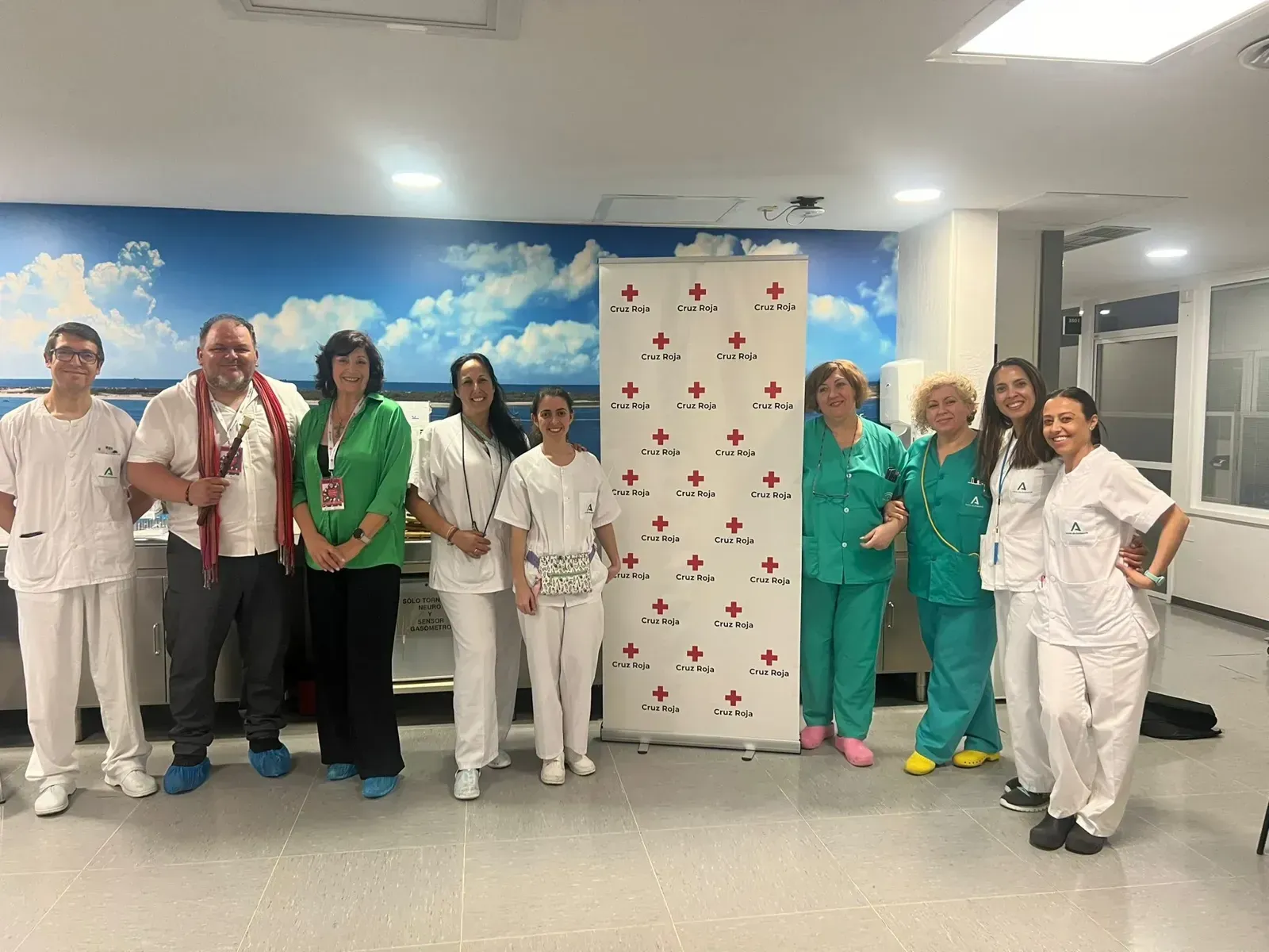 Grupo de personal médico de pie en el pasillo de un hospital junto a una pancarta, vestidos con uniformes quirúrgicos y blancos.