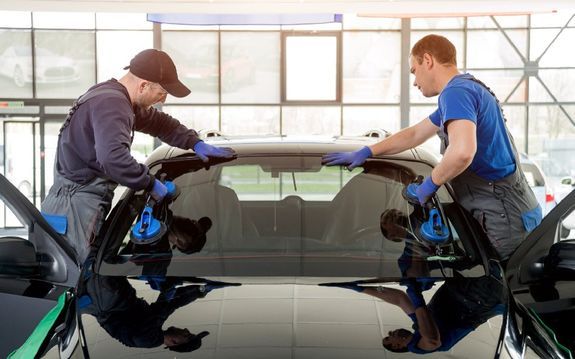 Autokorjaamon työntekijät vaihtamassa tuulilasia