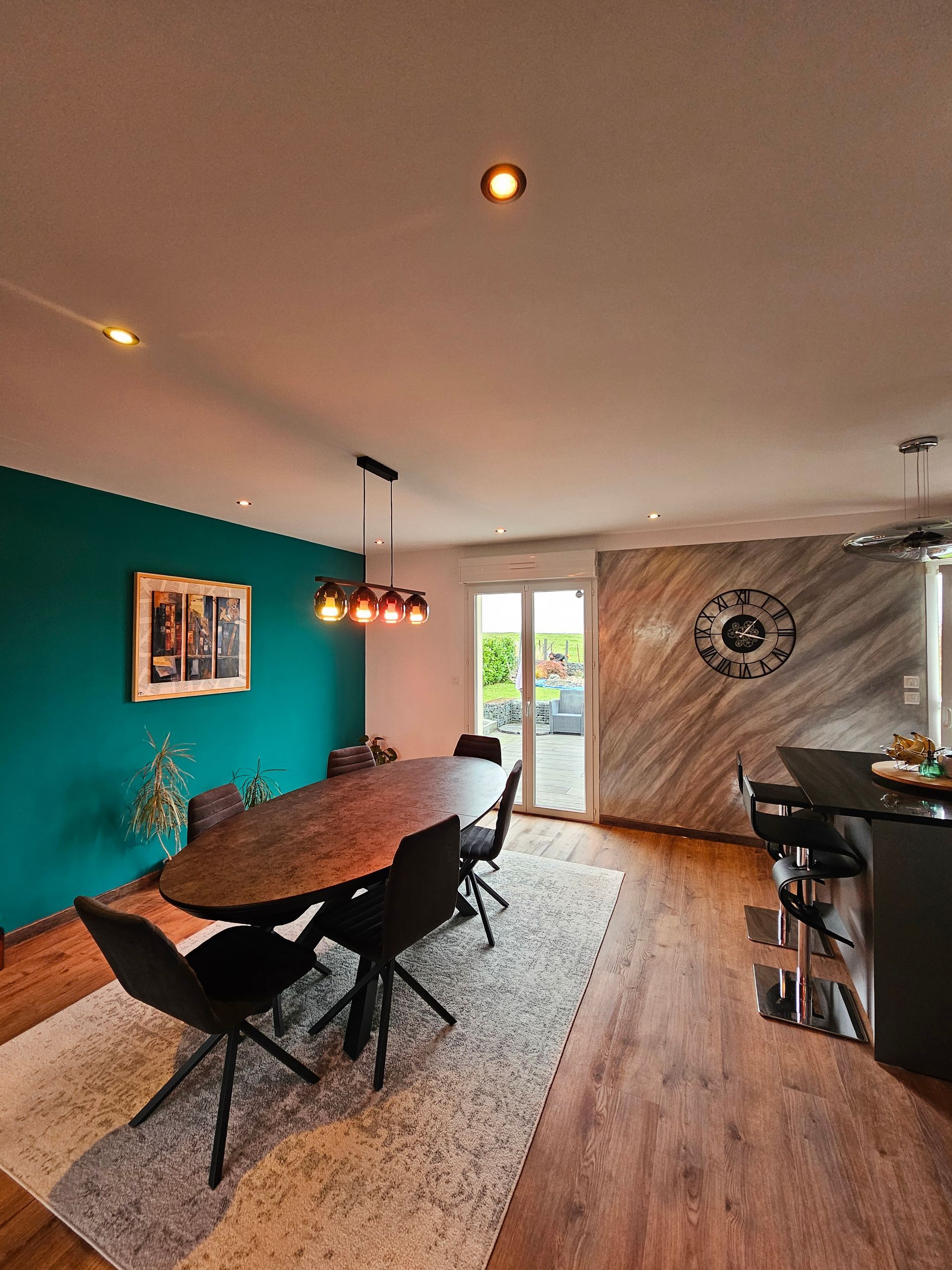 Salon avec une table ovale, un mur bleu canard et une vue sur une terrasse extérieur