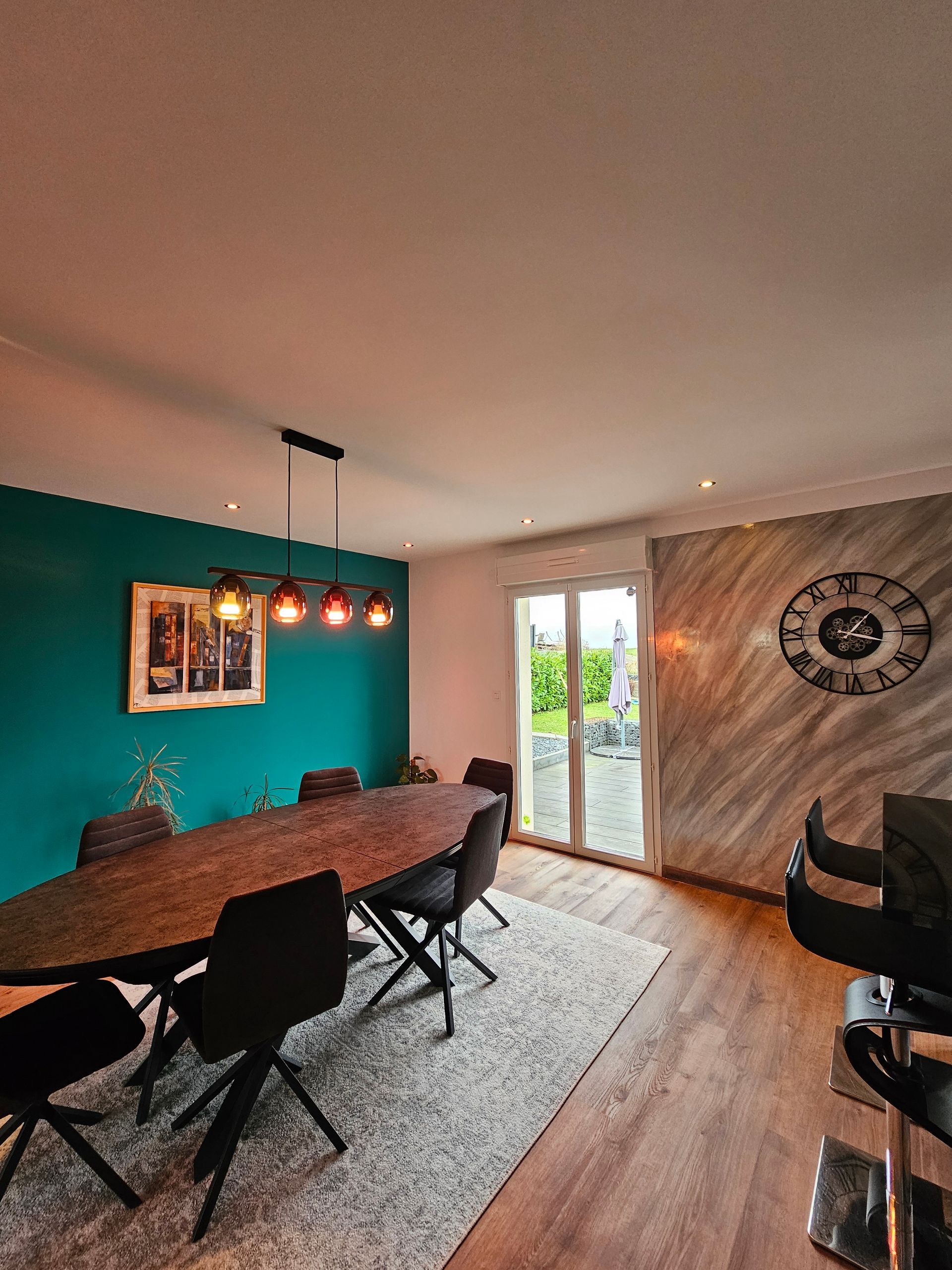 Table ovale avec des chaises design un mur bleu canard et un mur texturé gris et blanc