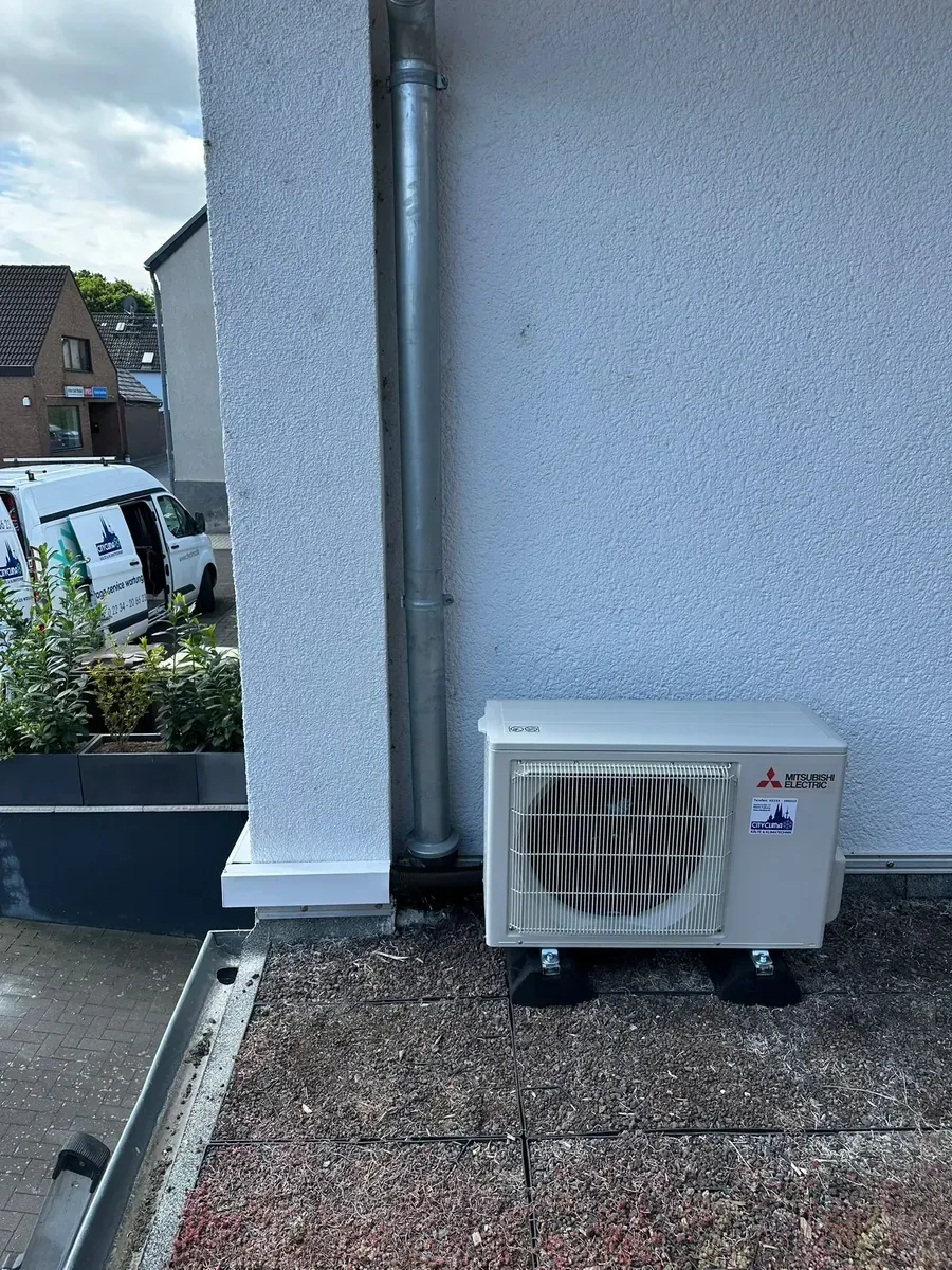 Außenwärmepumpeneinheit neben einer Hauswand auf einer gepflasterten Terrasse.