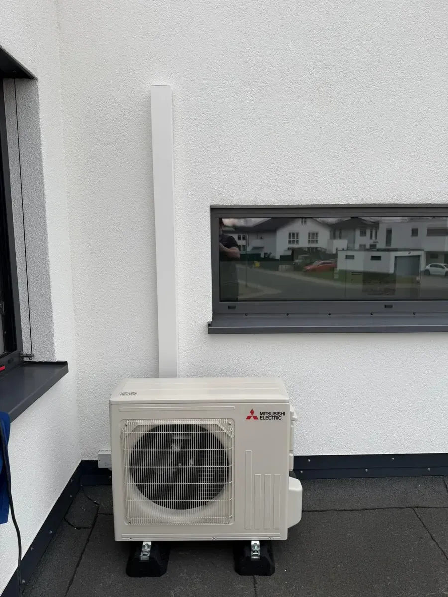 Mitsubishi-Außengerät für Klimaanlagen auf einem Balkon neben einem Fenster und einem Geländer.