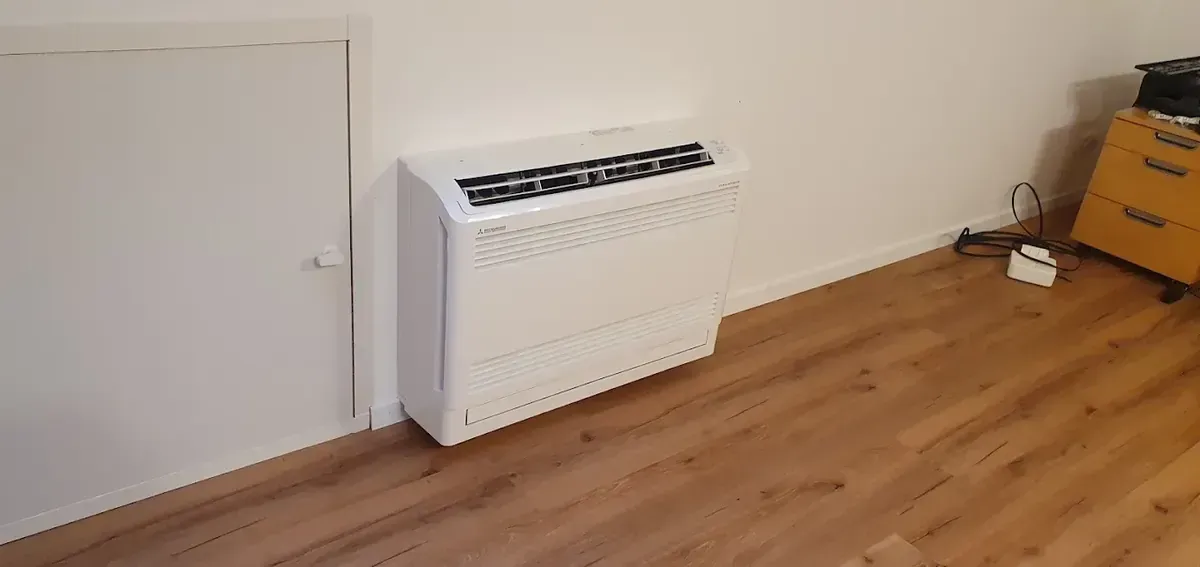 Kleiner Raum mit einer an der Wand montierten weißen Heizung und hellem Holzboden in der Nähe einer geschlossenen Tür.
