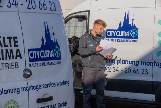 Mann in Arbeitskleidung liest Zeitung neben weißen Servicefahrzeugen mit CityClima-Logos.