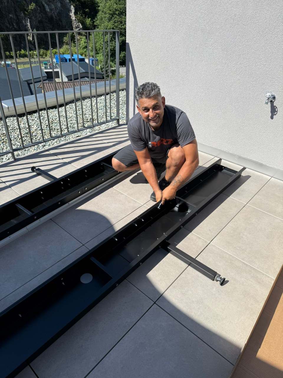 Uomo che monta una struttura in metallo nero su un patio piastrellato all'aperto, sorridente.