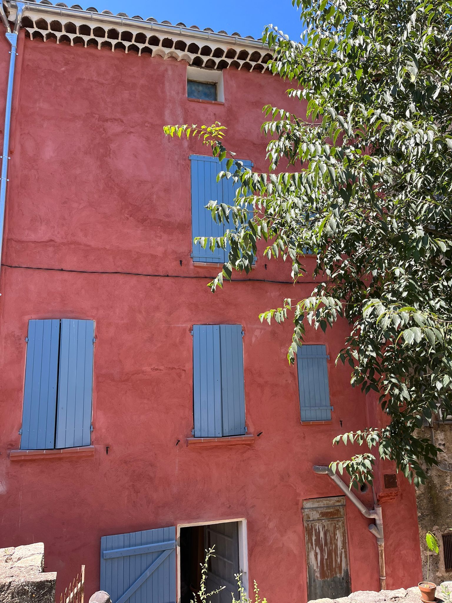 Façade extérieure en enduit rouge et volets bleus