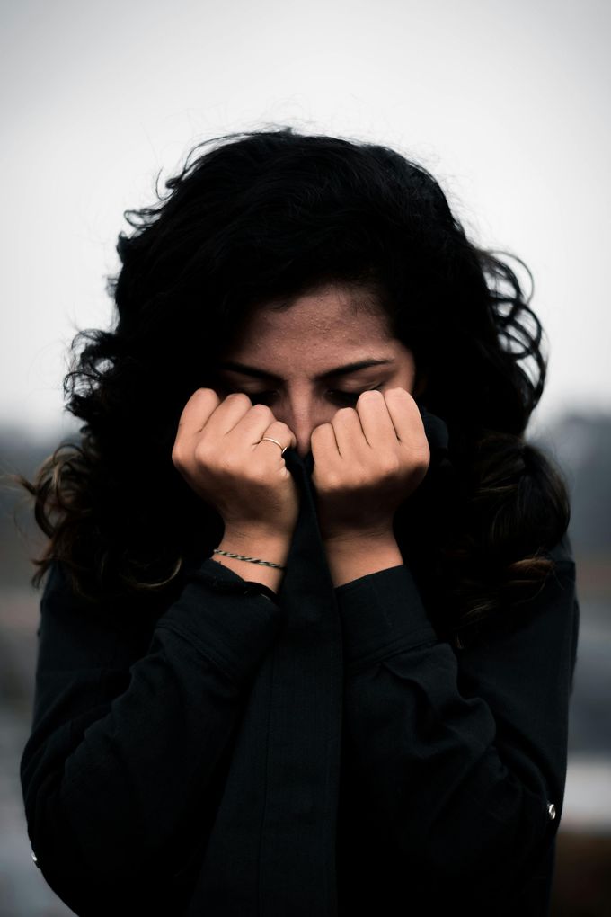 Una persona con cabello oscuro y rizado, que lleva una camisa oscura, se cubre la parte inferior del rostro con ambas manos.