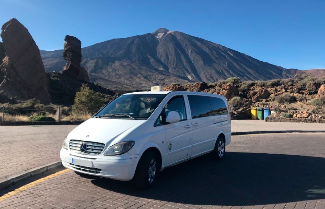 Una furgoneta blanca aparcada en un mirador pavimentado con agujas rocosas y una montaña bajo un cielo azul despejado.