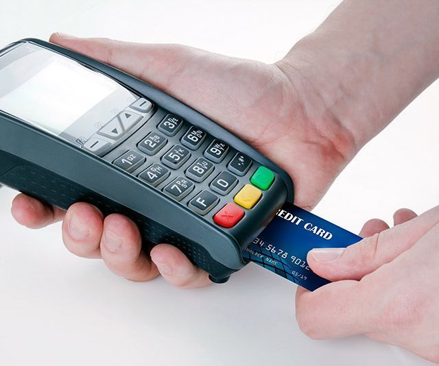 Una mano sostiene una tarjeta cerca de un terminal de pago para una transacción con tarjeta con chip.