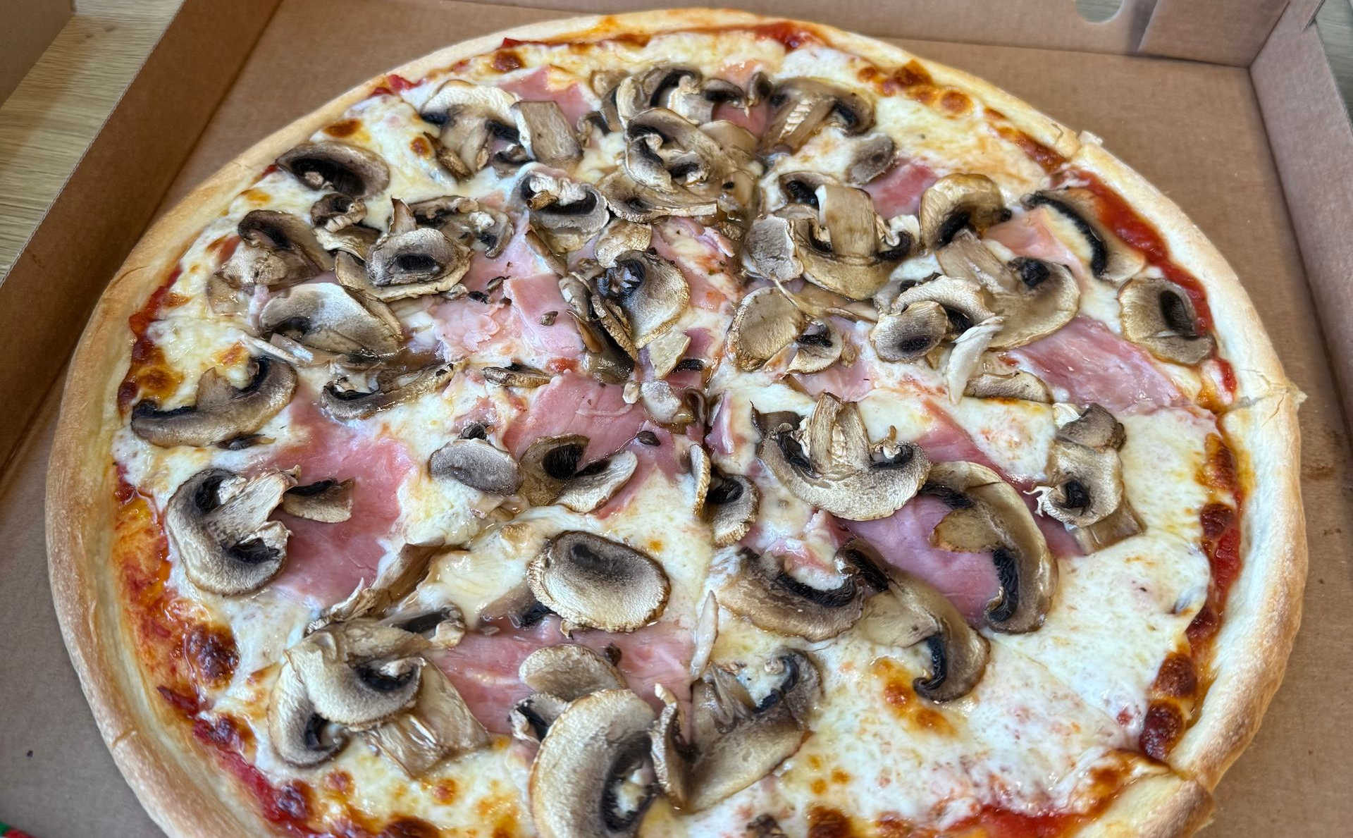 Pizza aux champignons et au jambon dans une boîte en carton, recouverte de fromage fondu et d'herbes.