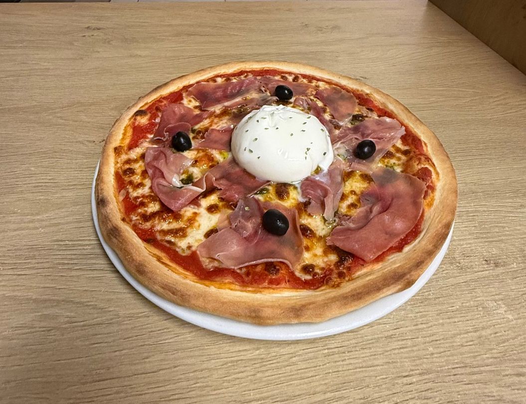 Pizza pepperoni garnie de basilic, servie sur une assiette à une table en bois.