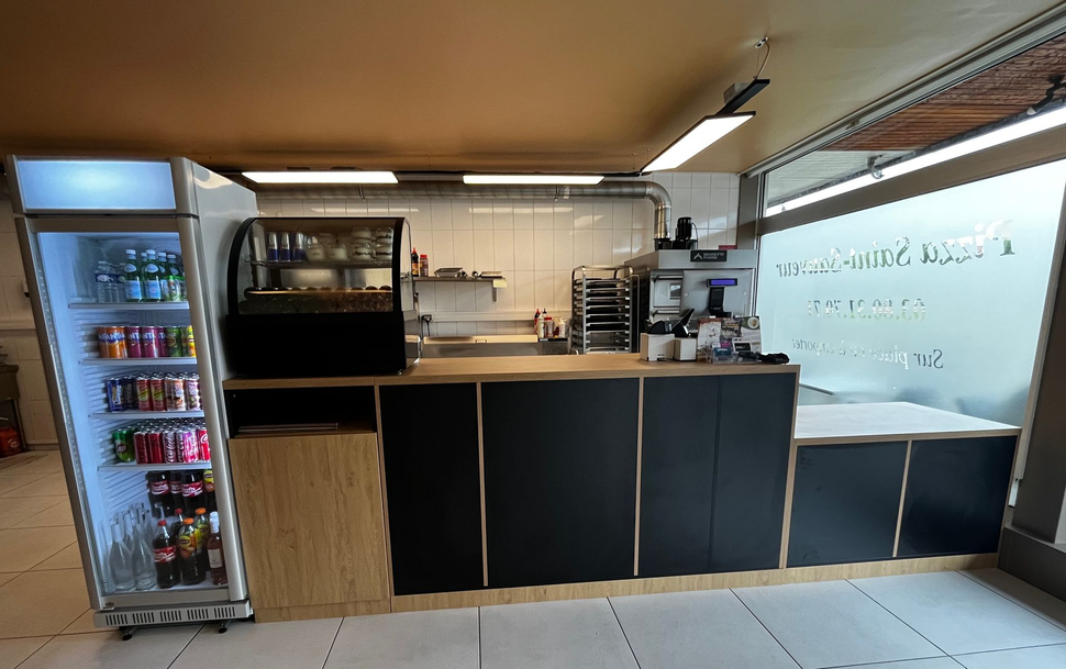 Comptoir de pizzeria moderne avec machine à café, réfrigérateur et tableau de menu sous un éclairage chaleureux