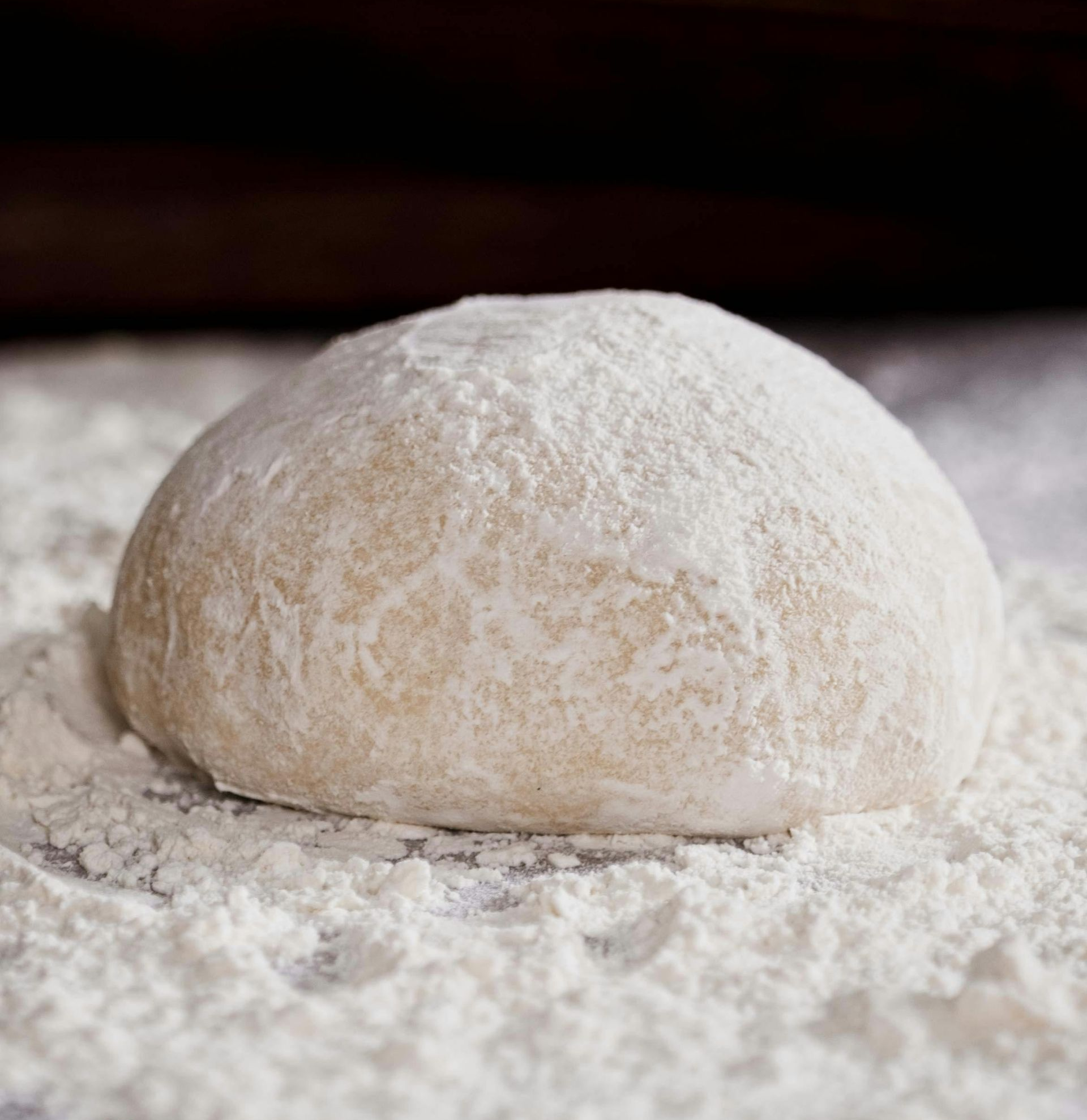 Boule de pâte farinée levant sur une surface légèrement saupoudrée de poudre, prête à être cuite
