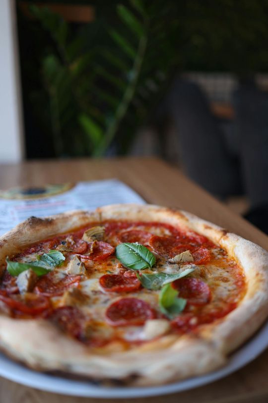 Pizza pepperoni garnie de basilic, servie sur une assiette à une table en bois.