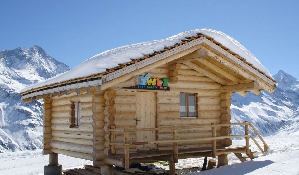 Cabane en bois dans un paysage de montagne enneigé, avec de la neige sur le toit.