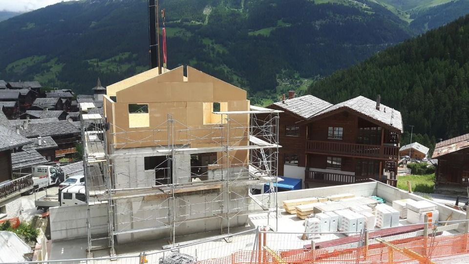 Construction d'une maison avec une base en béton et des étages supérieurs en bois, avec la montagne en arrière-plan.
