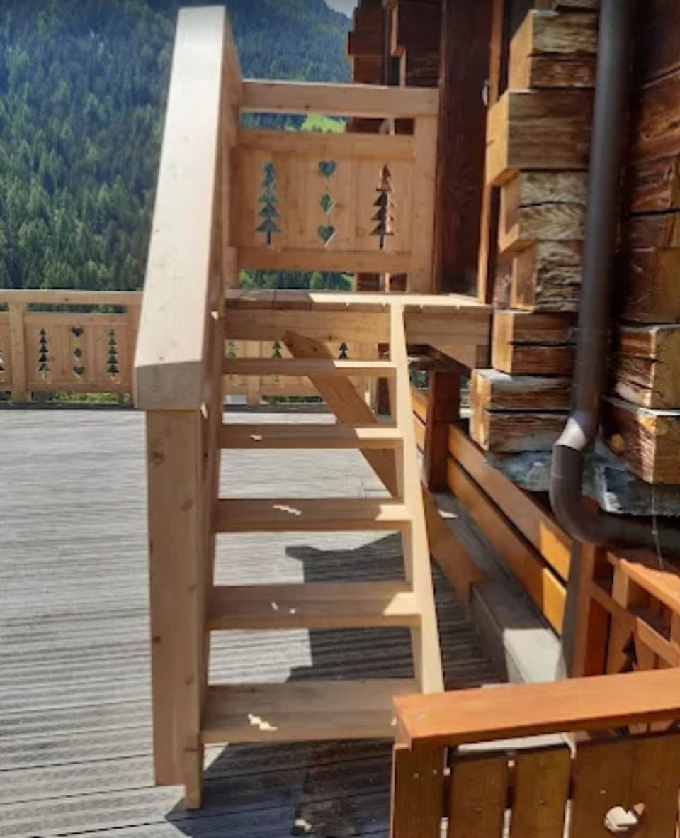 Escalier extérieur en bois avec rambarde décorative sur une terrasse en bois.