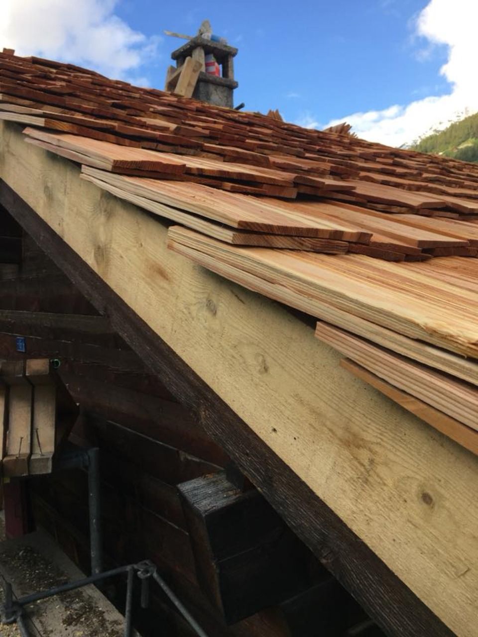 Gros plan sur une toiture en bois en construction ; des bardeaux de cèdre sont installés sur les chevrons, sous un ciel nuageux.