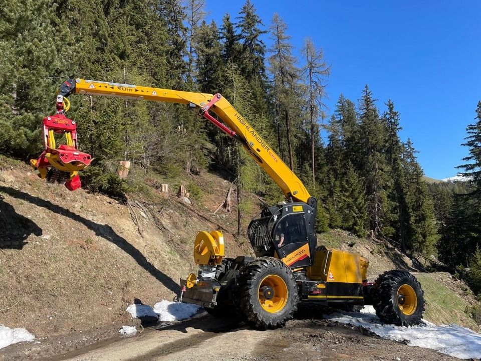 Machine forestière jaune avec bras de grue sur un flanc de colline, tenant une tête d'abattage, journée ensoleillée.
