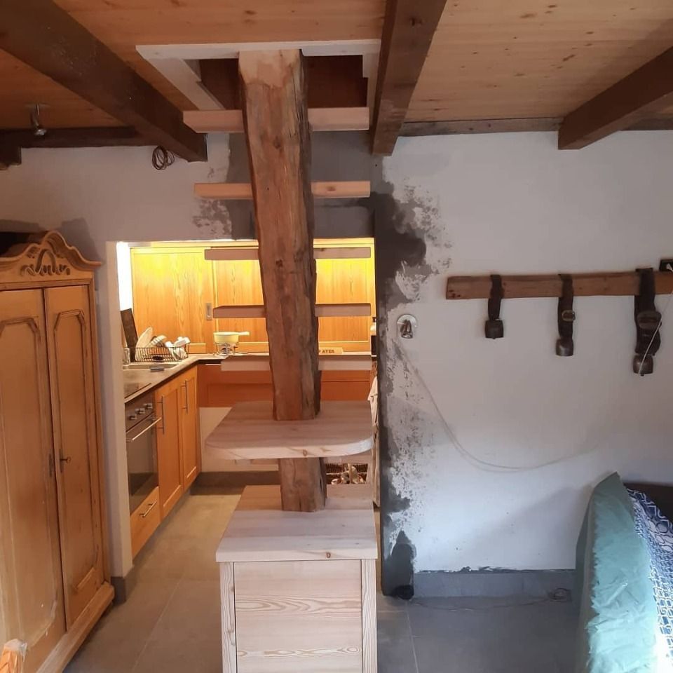 Escalier en bois avec étagères intégrées dans un intérieur rustique. Cuisine avec placards en arrière-plan.