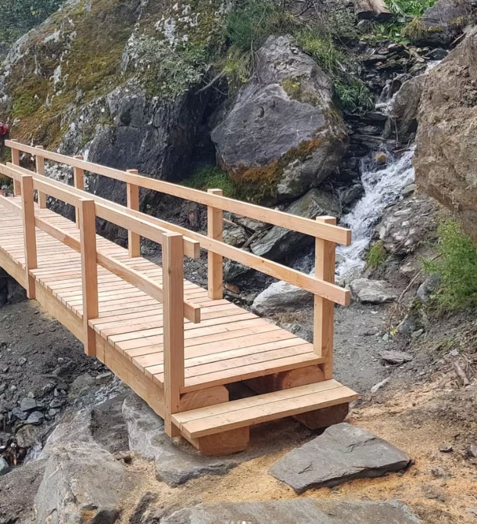 Pont en bois avec rambarde enjambant une petite cascade et des rochers.