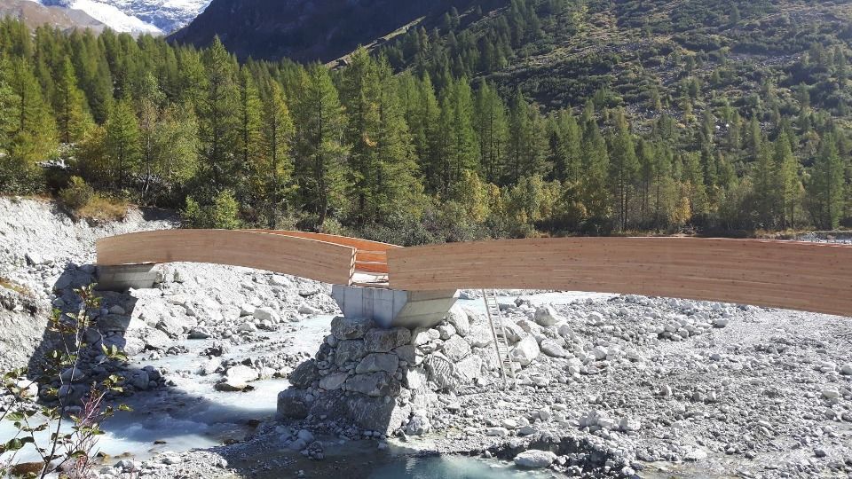 Pont endommagé enjambant une rivière dans un cadre forestier montagneux.