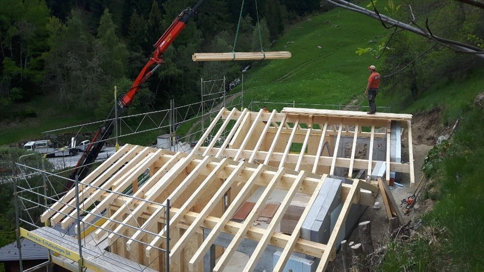 Construction d'une charpente de toit : une grue soulève une poutre en bois. Un ouvrier se tient sur le toit.